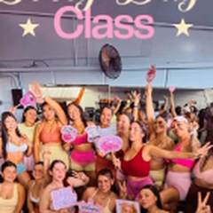 Foto de grupo de una Booty Day Class: las participantes con carteles rosados frente al espejo del estudio