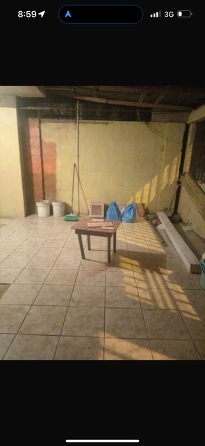 El local todavía vacío antes de remodelar: piso de baldosa, paredes sin pintar y una mesa suelta en el fondo
