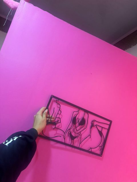 Instalando sobre la pared rosada el cuadro de línea negra que hoy recibe a las clientas