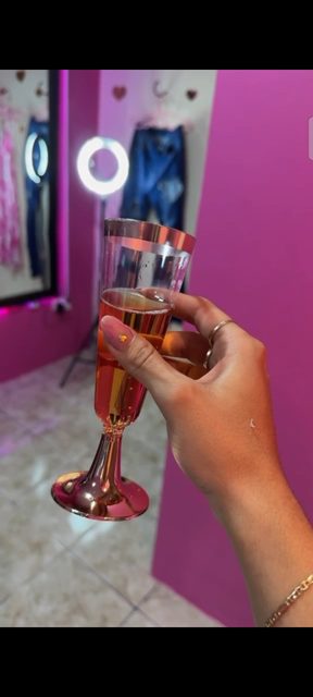 Una copa levantada para brindar el día de la apertura, con el neón rosa de la tienda de fondo