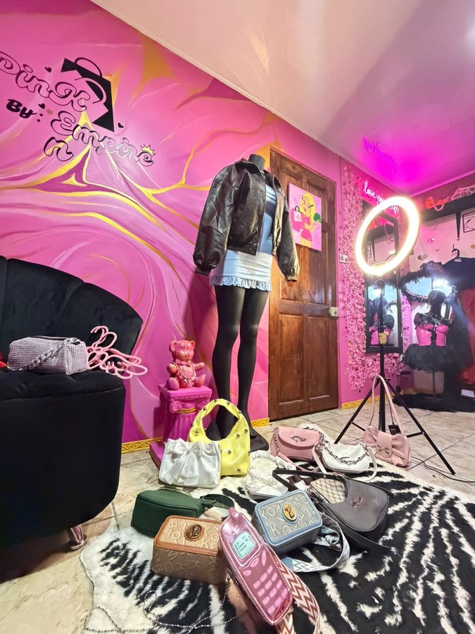 El maniquí frente al mural rosa pintado a mano, con el aro de luz y los bolsos alrededor