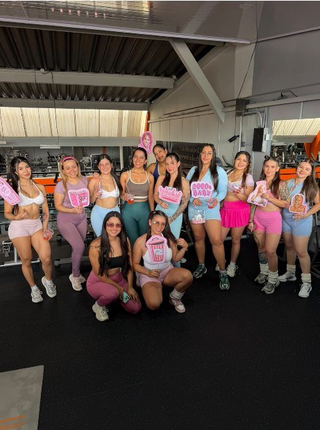 Grupo de clientas de PinKempire posando en el gimnasio con carteles rosados después del evento Glitter Gains