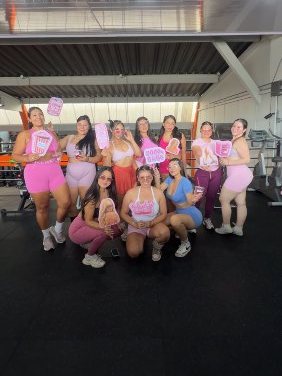 Clientas de PinKempire juntas en el gimnasio con ropa deportiva rosada y carteles del evento Glitter Gains